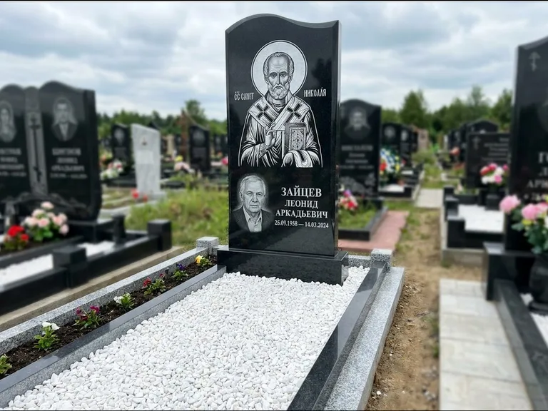 Памятник с гравировкой иконы: стела с крестообразным навершием — икона в резной рамке-киоте, газон без ограды, стриженая трава, работа «Раевская» в Ханты-Мансийске