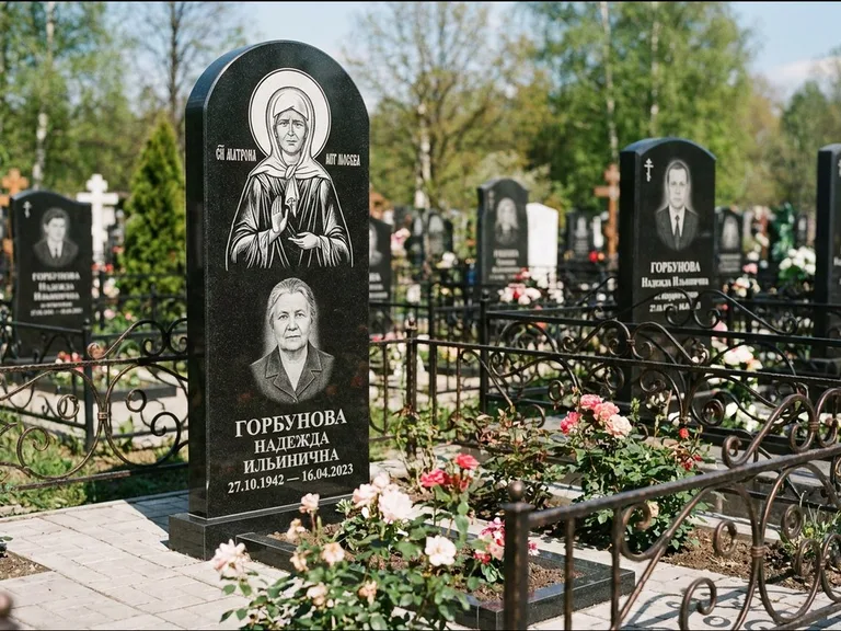 Памятник с гравировкой иконы: стела с арочным верхом и киотом под образ — гравировка образа Матроны Московской, гранитный цоколь с тёмной плиткой, работа «Ковалёв» в Ханты-Мансийске