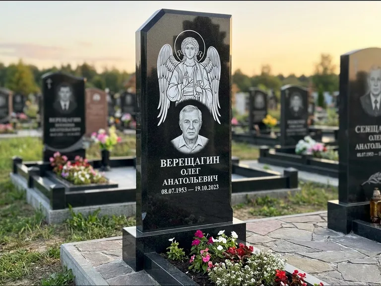 Памятник с гравировкой иконы: стела с резным навершием и нимбом в золоте — гравировка образа Спасителя, высокие разросшиеся туи полукругом, работа «Мельникова» в Ханты-Мансийске