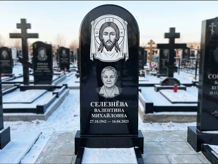 Памятник с гравировкой иконы: небольшая скромная одиночная стела с именной иконой — золочёный нимб на образе, аккуратный участок с газоном, работа «Ковалёв» в Ханты-Мансийске