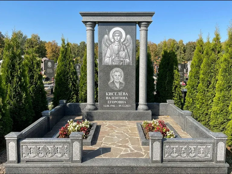 Памятник с гравировкой иконы: массивная стела с двускатным навершием-домиком — гравировка Николая Чудотворца, живая изгородь из туи, работа «Журавлёв» в Ханты-Мансийске