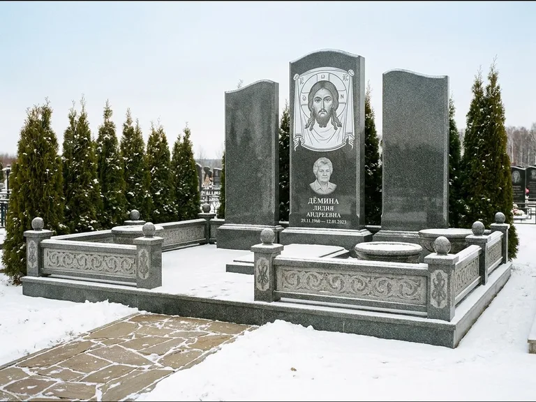Памятник с гравировкой иконы: узкая вертикальная стела-пилон с ликом — икона в резной рамке-киоте, открытая лужайка без ограды, работа «Одинцов» в Ханты-Мансийске