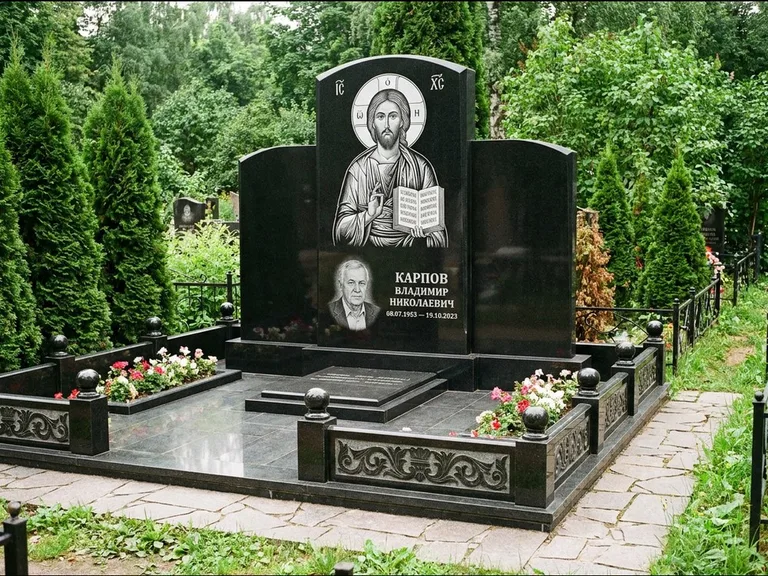 Памятник с гравировкой иконы: широкая панорамная стела с золочёным нимбом — гравировка образа Матроны Московской, цветник с белыми хризантемами, работа «Мельникова» в Ханты-Мансийске